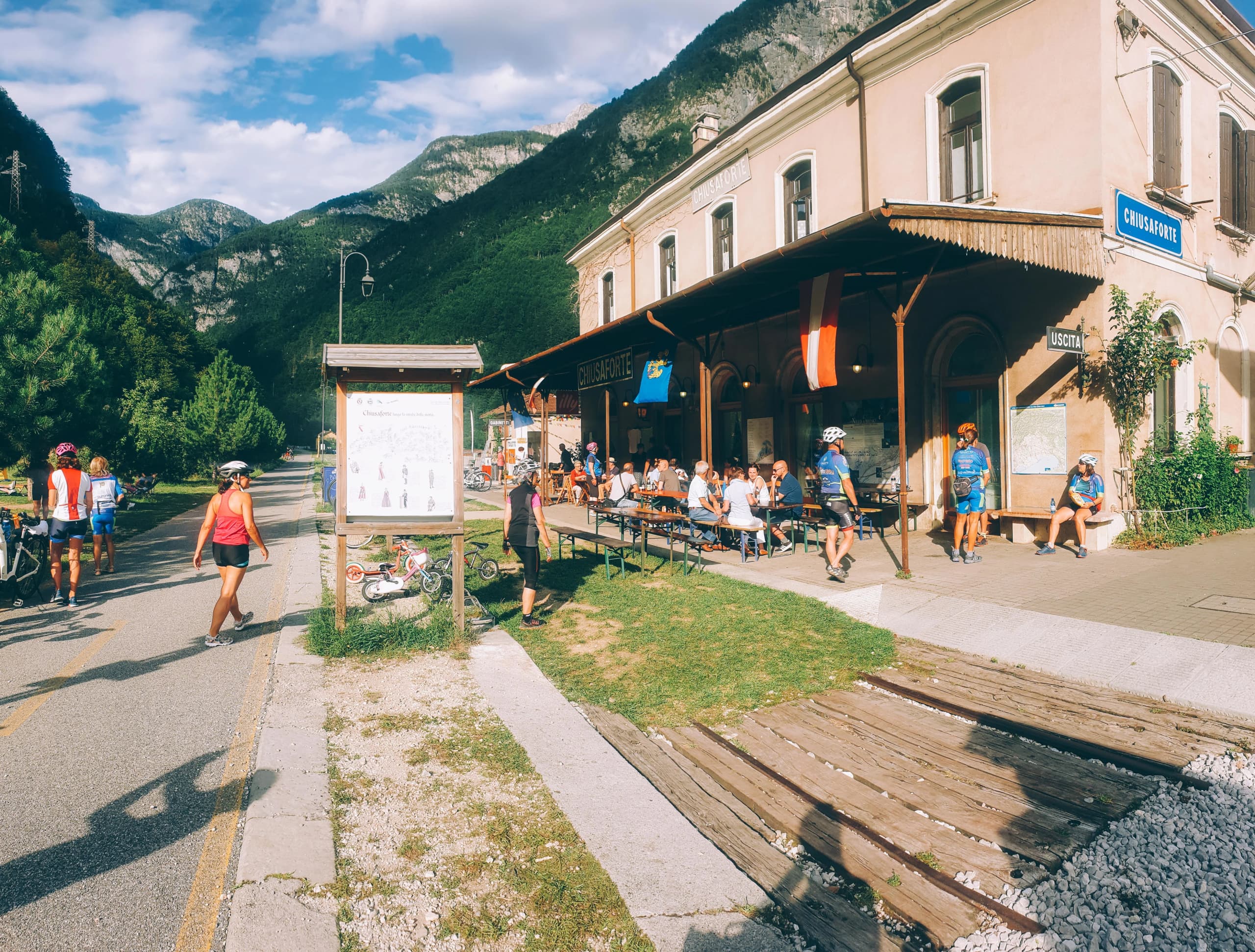 Gruppo di ciclisti in sosta davanti a una vecchia stazione ferroviaria ristrutturata a Chiusaforte, Friuli.